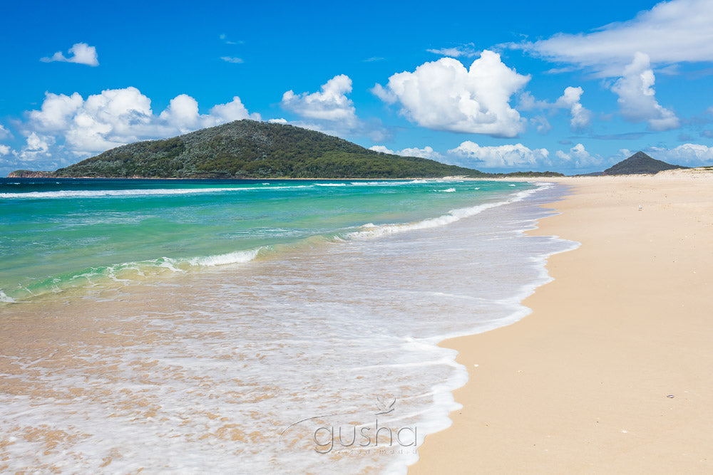 Photographed on the sands of Bennetts Beach, cumulus clouds float slowly behind Yacaaba Headland.