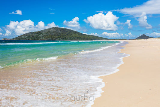 Photographed on the sands of Bennetts Beach, cumulus clouds float slowly behind Yacaaba Headland.