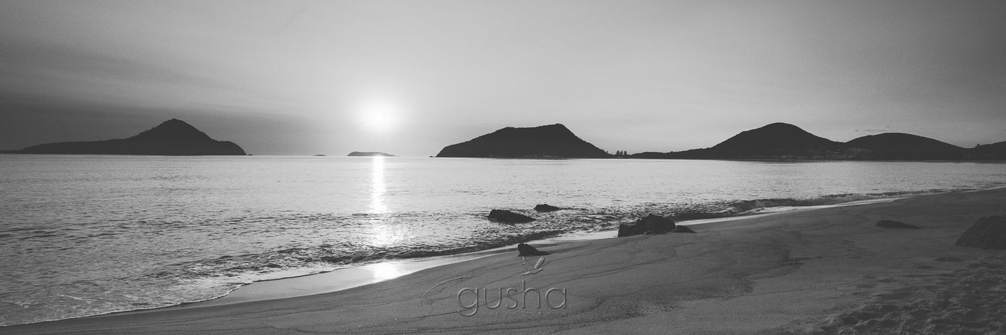 Sunrise silhouettes the heads of Port Stephens from the sands of Shoal Bay.