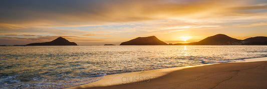 A warm sunrise silhouettes the heads of Port Stephens captured from the shoreline of Shoal Bay.