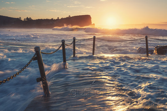 A photo of ocean water rushing over Avalon Beach pool at sunrise in Sydney, Australia.