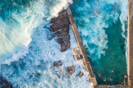 An overhead photo of large surf crashing over the pool and swimmers at Avalon Pool in Sydney, Australia.